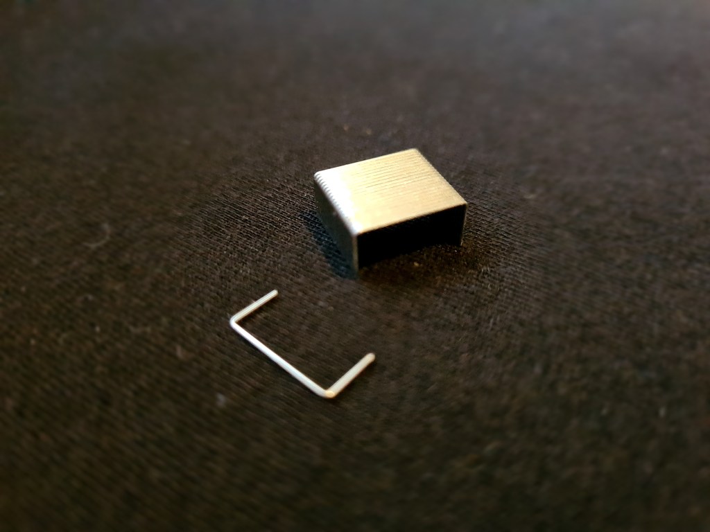 A clump of staples and a single staple, on a black cloth.